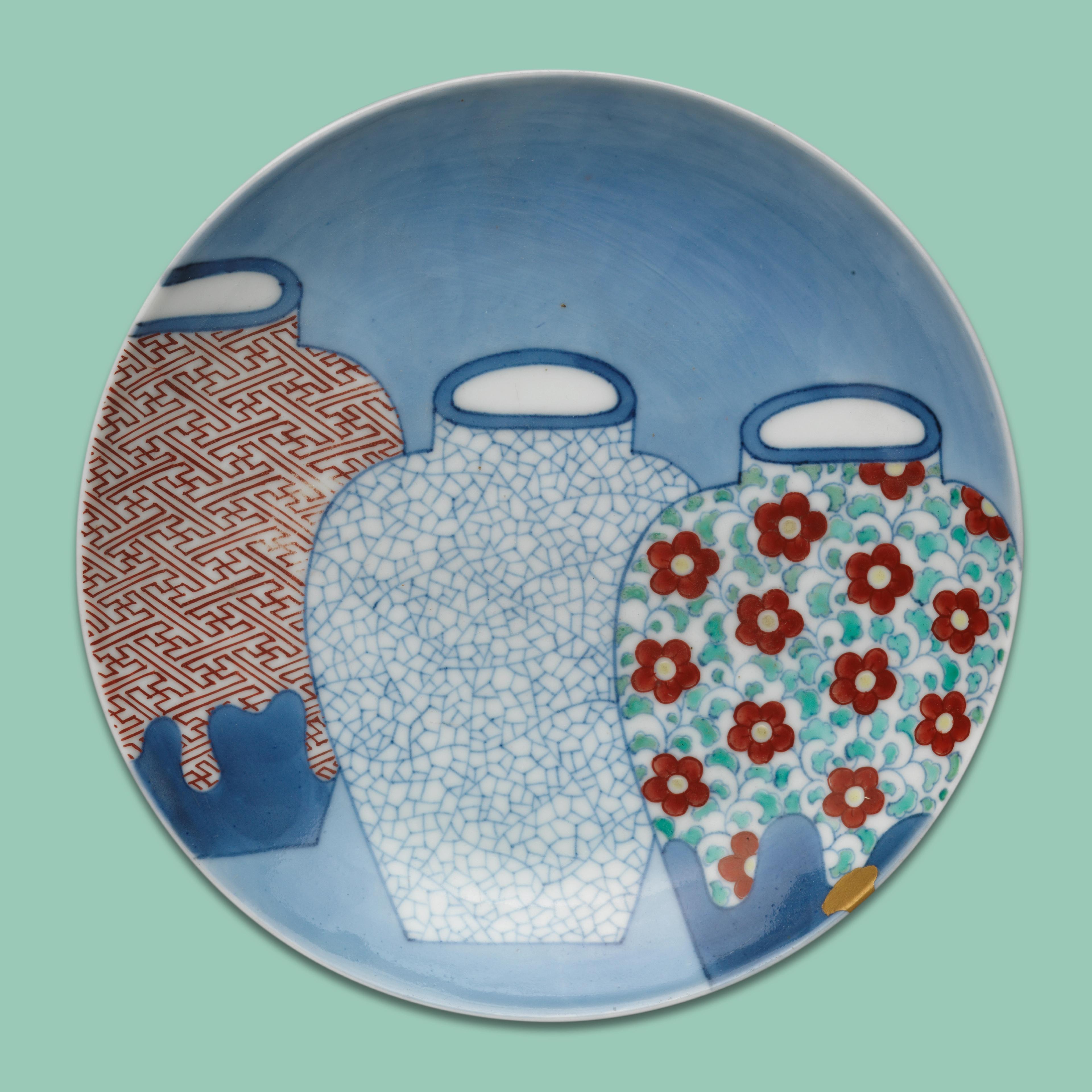 Ceramic plate with three overlapping vases. Left vase has red geometric patterns, middle is white with blue cracks, and right has red flowers on light blue.