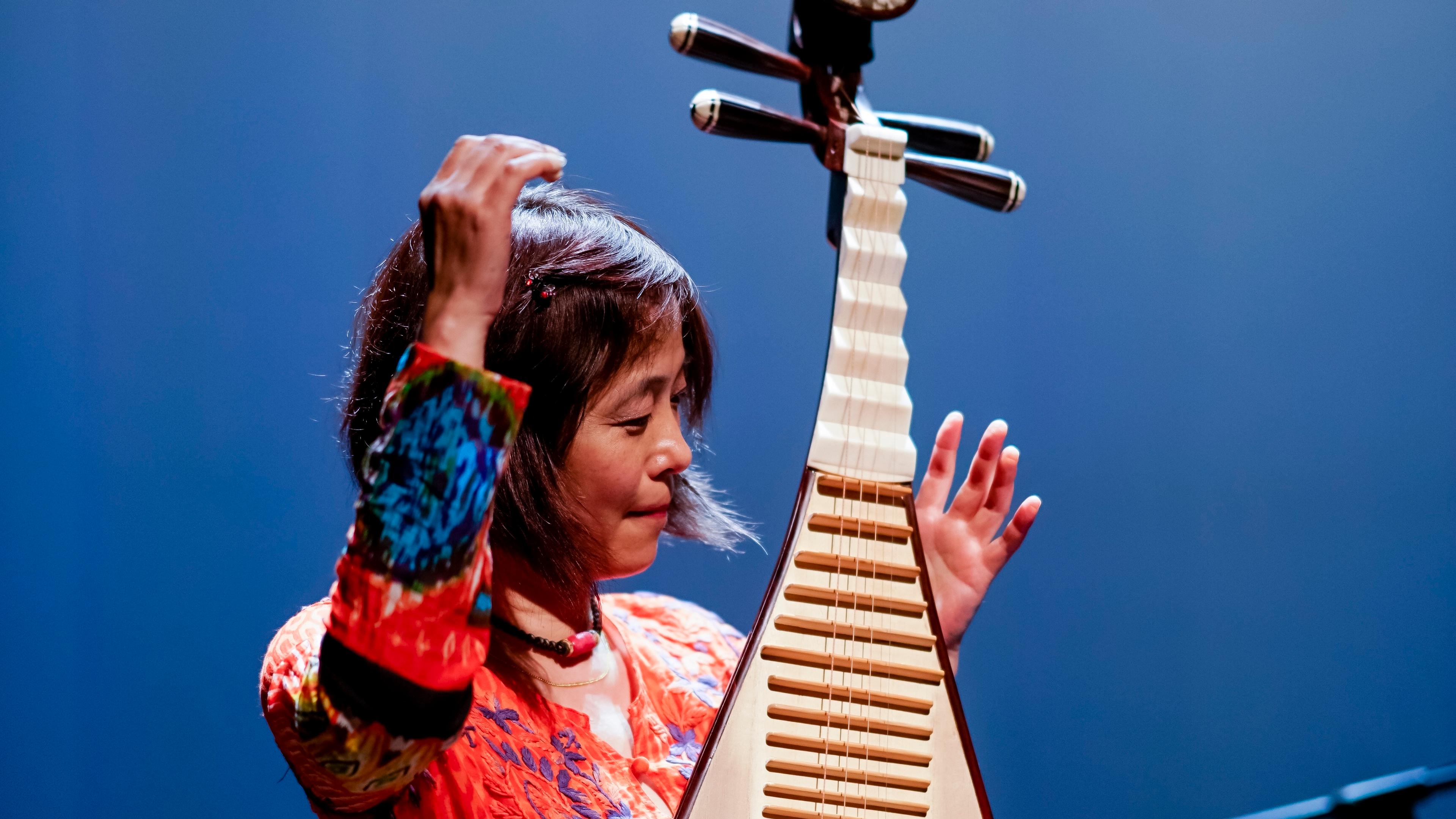 A woman wearing red plays a pipa (a type of Chinese lute).