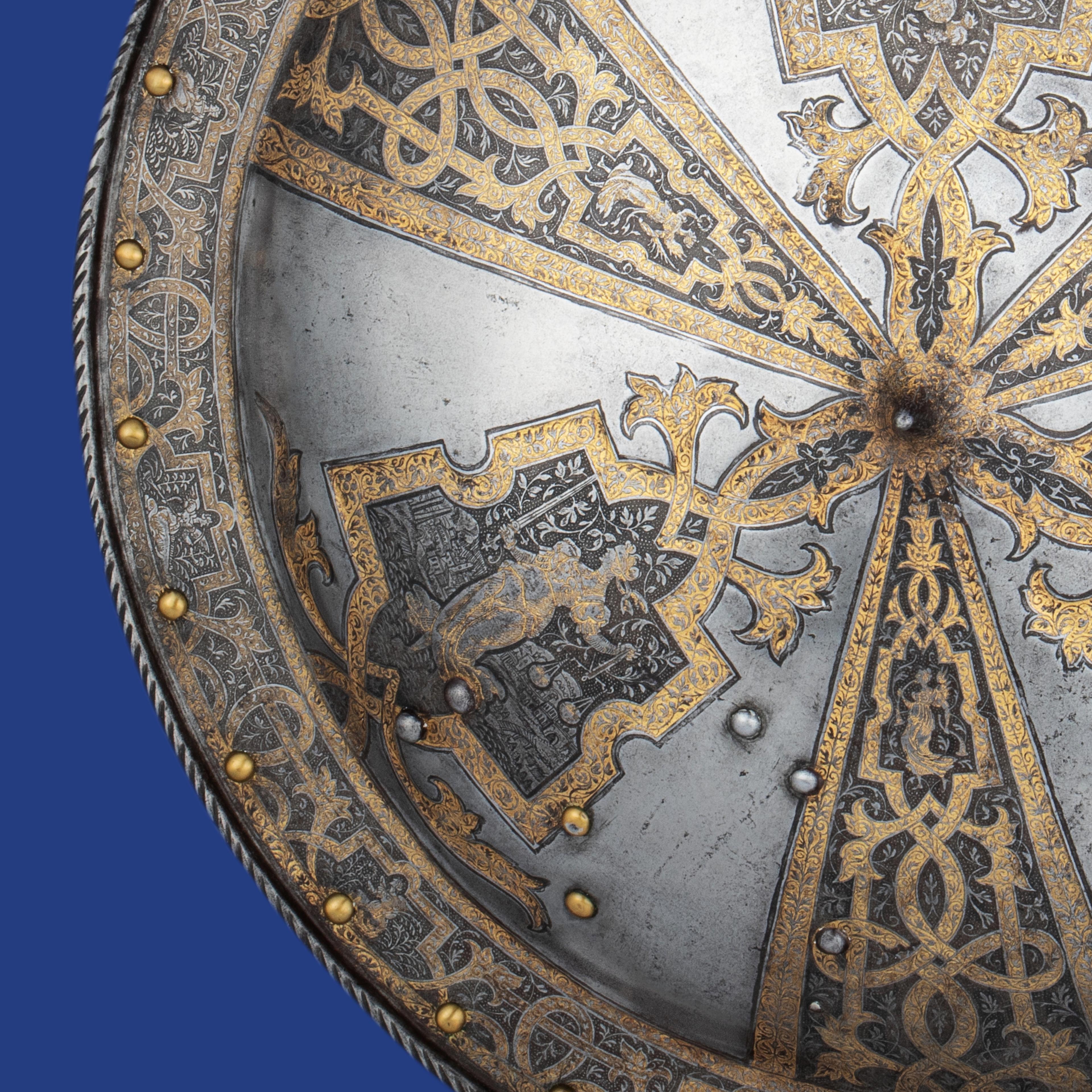 Ornate silver shield with intricate gold vine patterns and medieval animal motifs, accented by brass rivets on a blue background.