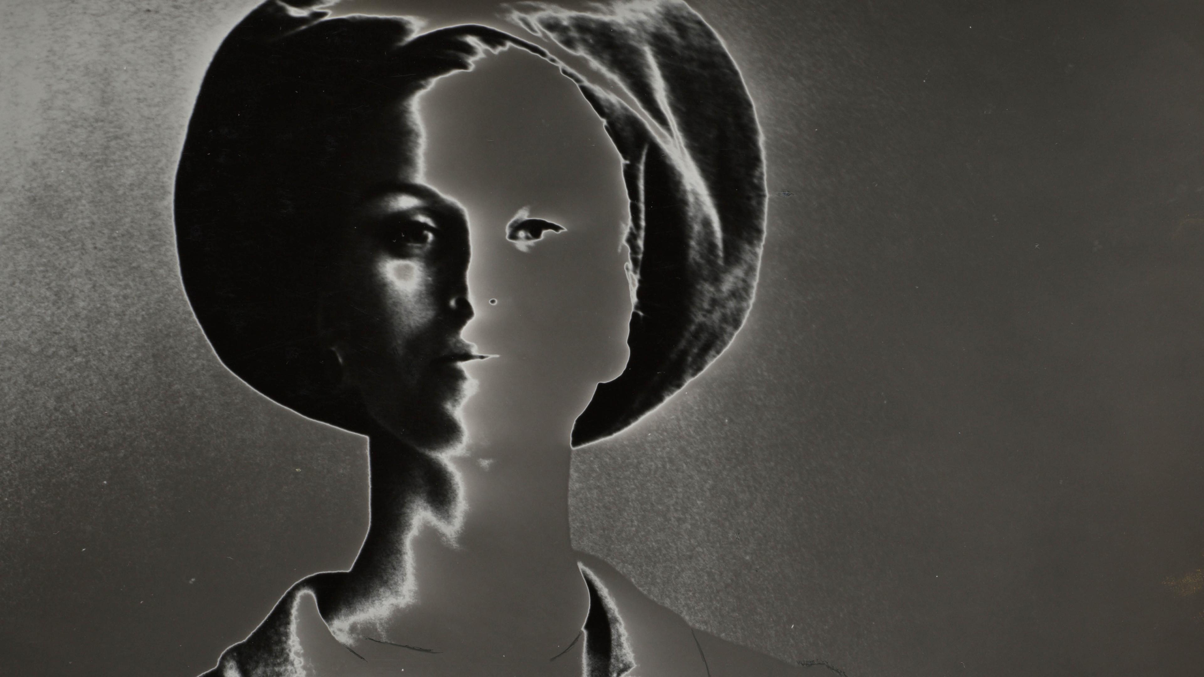 A stylized black-and-white image of a person wearing a hat and jacket, with high contrast and negative effect