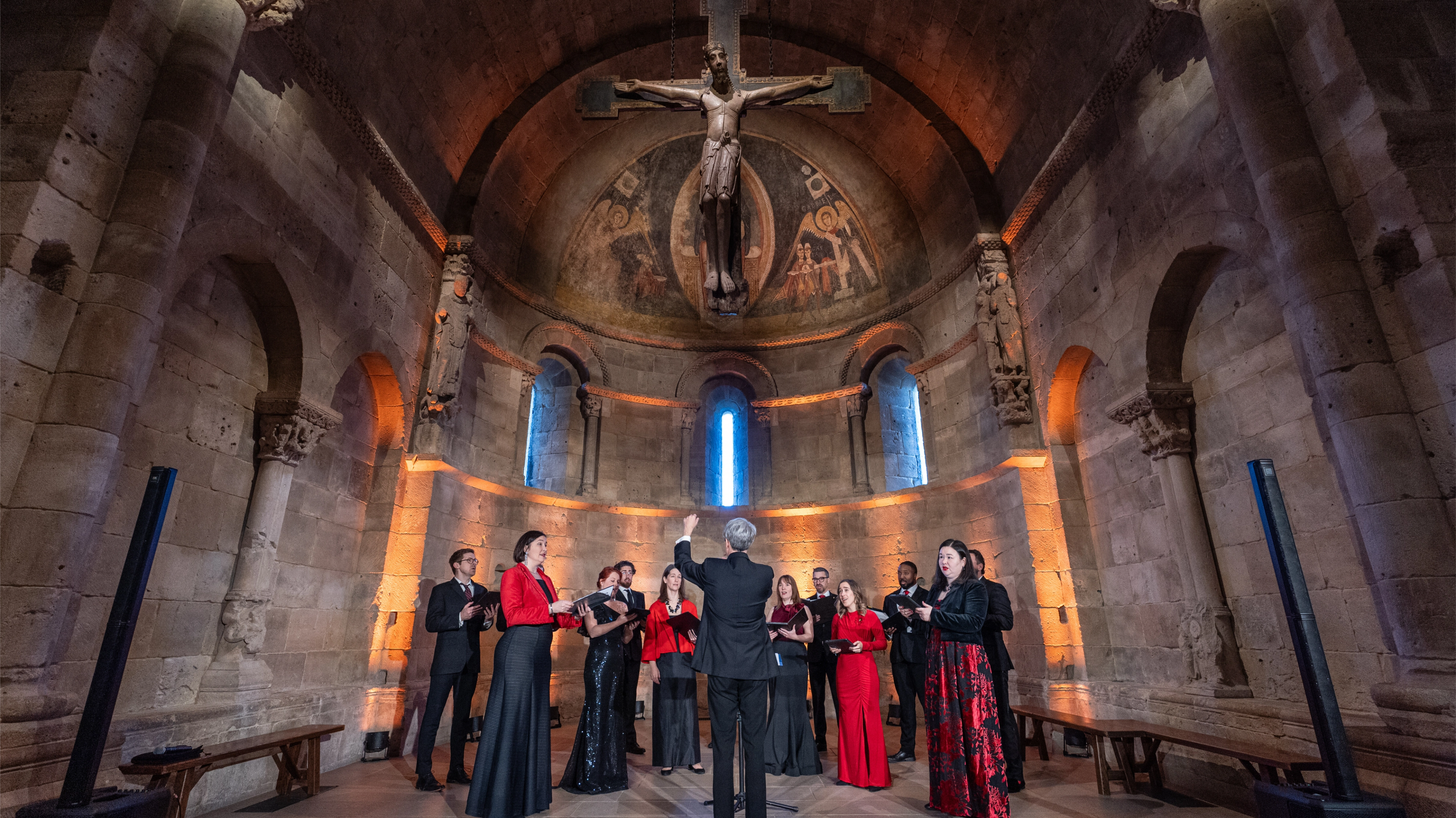 A choir stands in the Fuentidueña Chapel, beneath a crucifix.