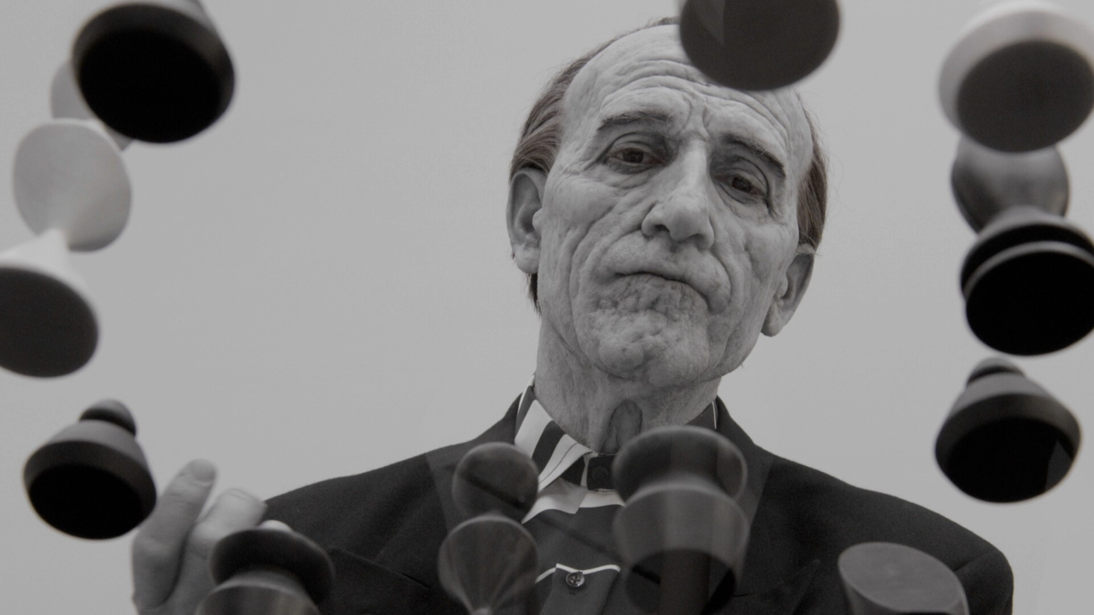 A seemingly old man surrounded by a ring of pegs.