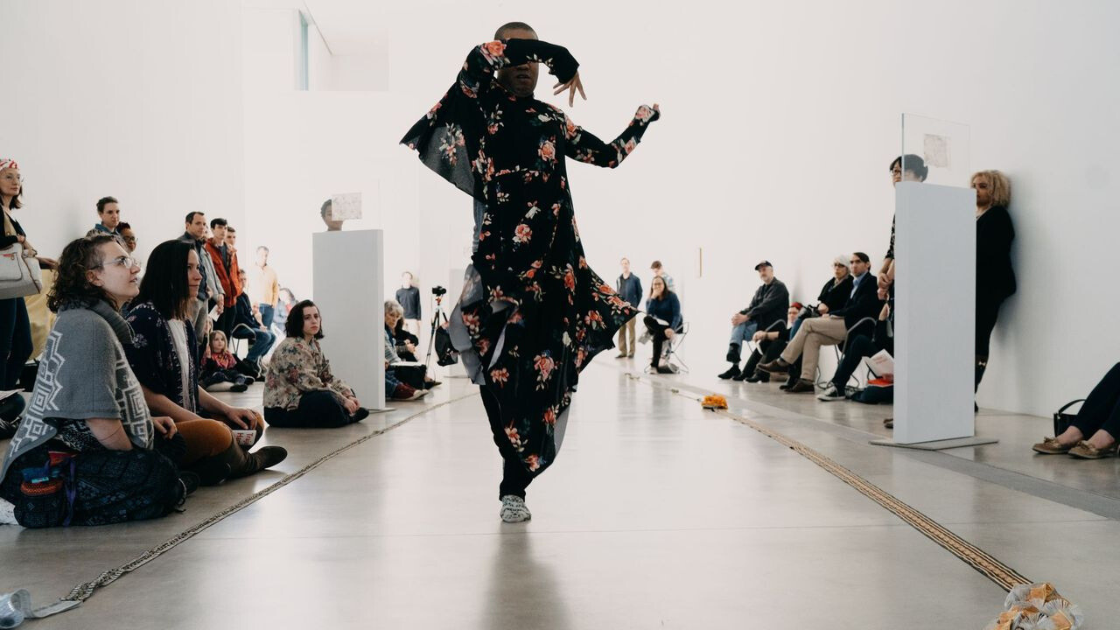 A person in a floral gown dances in a white room.