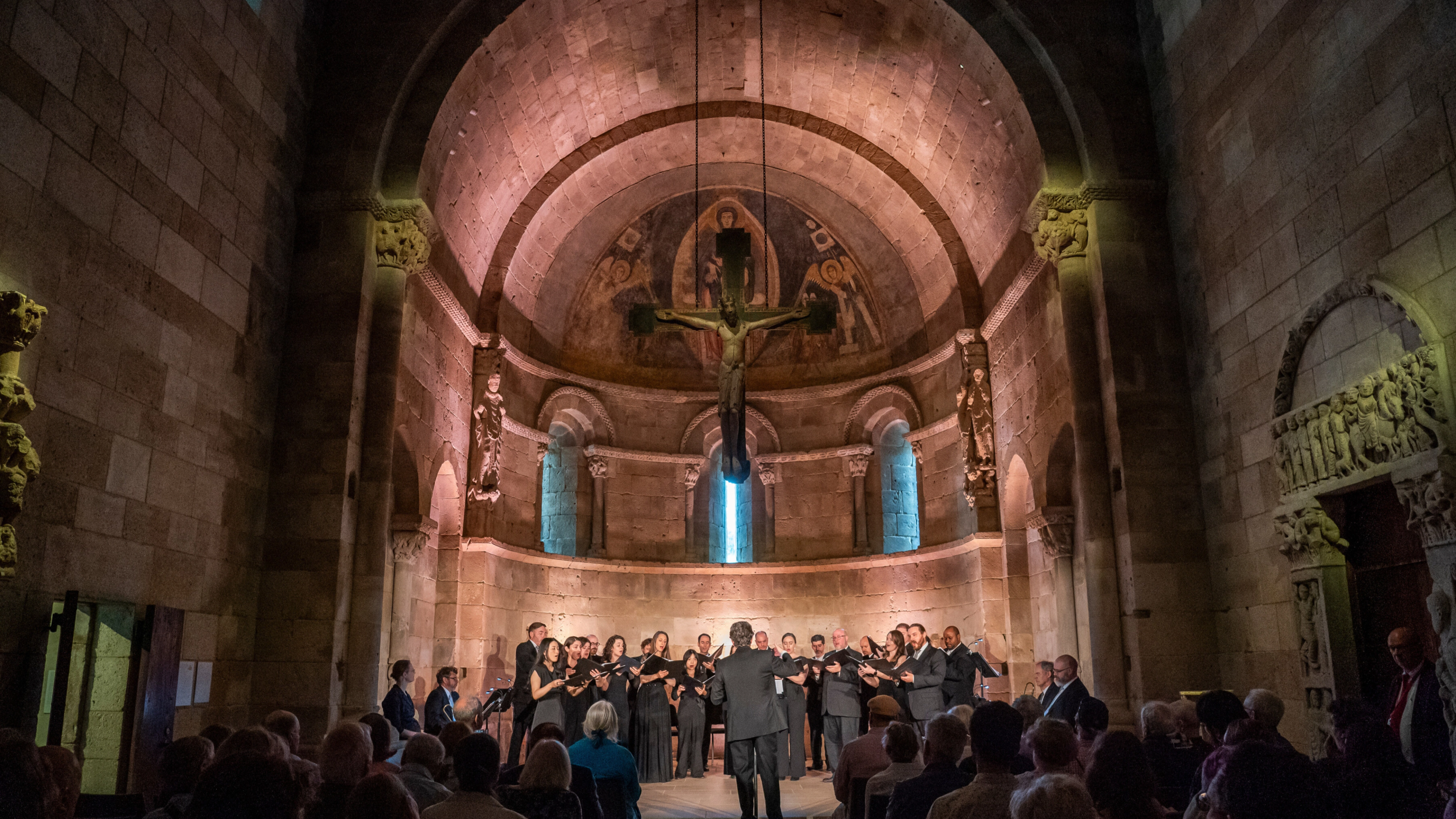 A choir stands in the Fuentidueña Chapel, beneath a crucifix.